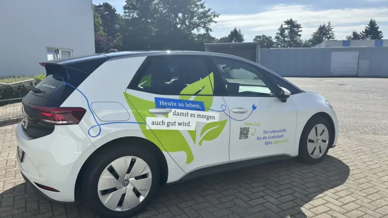 Weißes Elektroauto mit hellgrüner Teilfolierung, Schriftzug und QR-Code auf der Beifahrertür