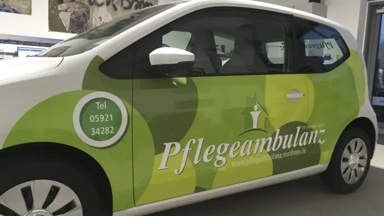 Weißer Kleinwagen mit großflächiger grüner Folierung, Schriftzug und Telefonnummer