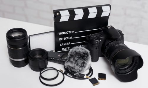 videography and photography equipment - modern dslr camera, lenses, filters, microphone with windscreen, led light, memory cards and clapper board on white table background